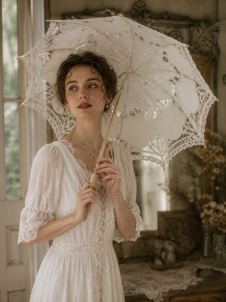 May include: A white lace parasol with intricate floral patterns and scalloped edges, featuring a light-colored wooden handle and central shaft. The parasol is held open, displaying a delicate, semi-sheer fabric construction with detailed embroidery.