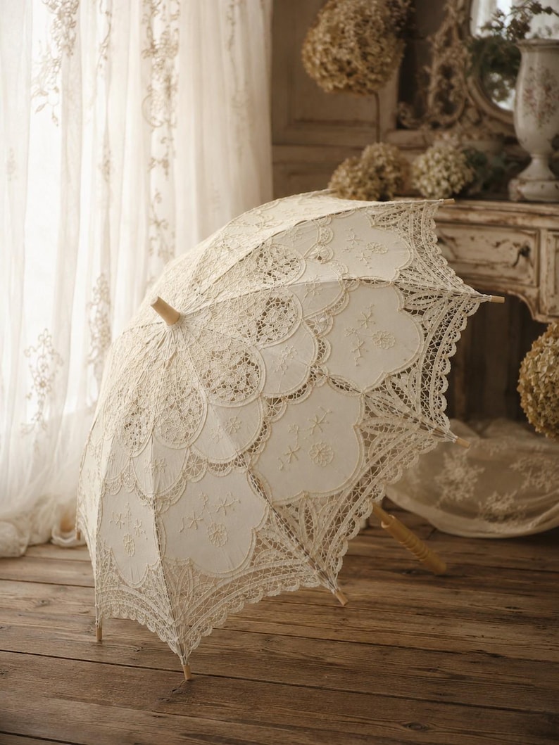 May include: An off-white lace parasol featuring intricate scalloped edges, detailed floral embroidery, and a light-colored wooden handle. The canopy is constructed with layered fabric panels and delicate needlework patterns throughout the design.