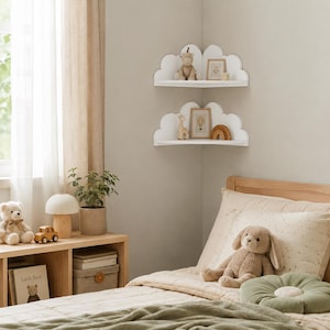 May include: Two white corner shelves shaped like clouds mounted on a wall. The top shelf holds a small stuffed animal and a framed picture. The bottom shelf holds a small giraffe figurine, a framed picture, and a wooden rainbow arch decoration.