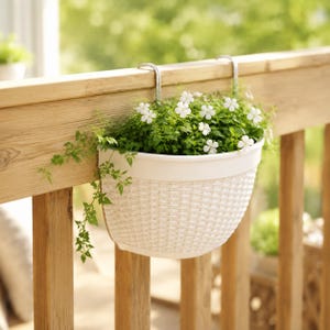 May include: A white, semi-circular hanging planter with a woven texture pattern. The planter features two silver-colored metal hooks attached to the top rim, allowing it to hang securely over a wooden railing. It is filled with green foliage.
