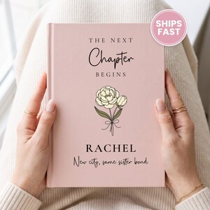 May include: A light pink hardcover journal featuring the text "THE NEXT Chapter BEGINS" in black, a line drawing of a flower bouquet, the name "RACHEL" in capital letters, and the phrase "New city, same sister bond" in script.