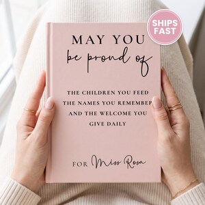 May include: A light pink hardcover book with black text that reads: MAY YOU be proud of THE CHILDREN YOU FEED THE NAMES YOU REMEMBER AND THE WELCOME YOU GIVE DAILY FOR Miss Rosa. The book cover features a mix of serif and script fonts.