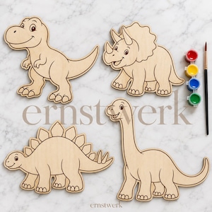 May include: Four unfinished wooden dinosaur cutouts including a T-Rex, Triceratops, Stegosaurus, and Brachiosaurus. A paintbrush and four small paint pots in red, yellow, blue, and green are included. The word ernstwerk is visible.