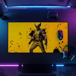 Peut inclure: Un tapis de bureau rectangulaire avec un fond jaune orné d'éclaboussures d'encre noire et une illustration centrale du personnage Wolverine portant un costume jaune et noir avec des griffes métalliques déployées aux deux mains.