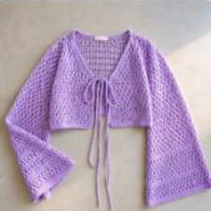 Peut inclure: Un cardigan en crochet violet clair à manches longues et ouverture frontale, doté d'une encolure en V et d'une fermeture à nouer avec deux longs cordons assortis. Le vêtement présente un motif en maille ajourée et des manches évasées.