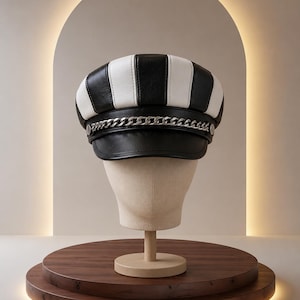 May include: A newsboy cap featuring alternating vertical panels of black and white material. The hat includes a black brim and a silver-toned metal chain detail that runs horizontally across the front, secured by circular silver-toned side accents.
