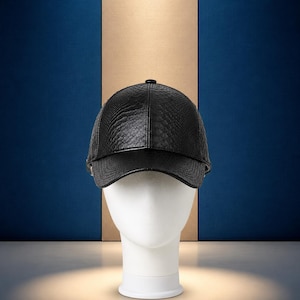 Pode incluir: Um boné de beisebol preto com um padrão texturizado semelhante a pele de cobra na copa e na aba curva. O boné é construído com um painel frontal estruturado e um pequeno botão no topo, apresentando um acabamento escuro e consistente.