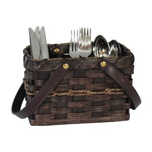 May include: A rectangular dark brown woven basket with a handle, featuring a decorative braided trim and gold-tone metal rivets. The basket contains stainless steel cutlery, including knives, forks, and spoons, organized in separate interior compartments.