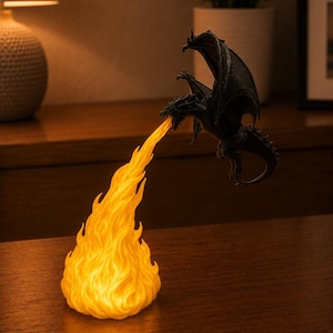May include: A dark gray dragon figurine in a flying pose, emitting a bright, glowing orange flame from its mouth. The flame is sculpted with detailed, textured waves and serves as a light source, casting a warm, vibrant glow against the dark dragon.