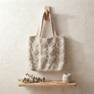 Pode incluir: Uma bolsa tote de crochê bege com um padrão de cestaria texturizado e duas alças integradas. A bolsa é feita de fio e exibe um design geométrico consistente e repetitivo em toda a superfície frontal da bolsa tote.
