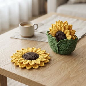 May include: A set of crochet sunflower coasters with yellow petals and a dark brown centre. One coaster lies flat on the surface, while others are stacked inside a green crochet holder shaped like a flower bud with textured leaves.