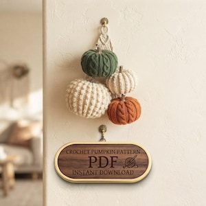 May include: A collection of four crocheted pumpkins in green, cream, and orange, hanging from a wall hook. Below, an oval wooden sign with a gold frame displays the text: CROCHET PUMPKIN PATTERN PDF INSTANT DOWNLOAD, featuring a yarn ball icon.