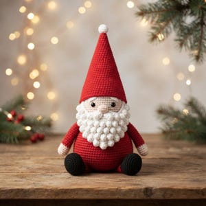 Peut inclure: Une figurine de Père Noël au crochet avec un grand bonnet pointu rouge surmonté d'un pompon blanc, un visage beige rond aux yeux noirs et une barbe blanche texturée faite de points noisette. Le corps est rouge avec des pieds noirs.
