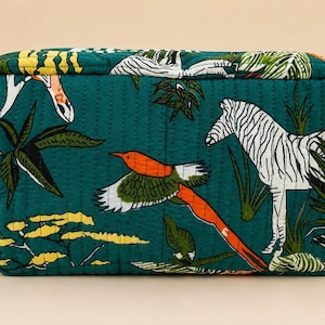 May include: A rectangular quilted pouch in deep teal featuring a vibrant print of a white zebra, a flying bird with orange and green wings, and yellow acacia-style trees. The fabric has vertical stitching and a small side handle.
