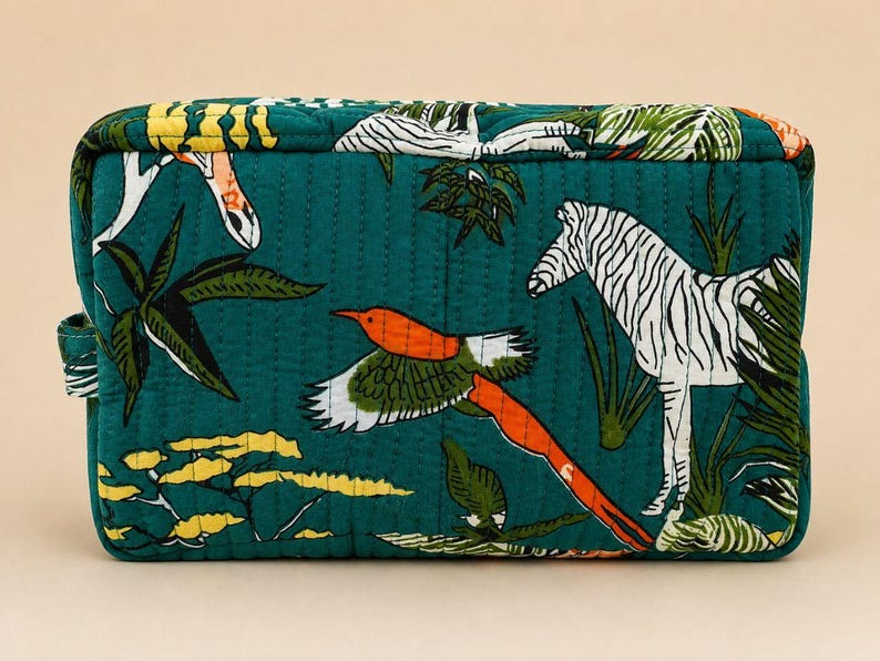 May include: A rectangular quilted pouch in deep teal featuring a vibrant print of a white zebra, a flying bird with orange and green wings, and yellow acacia-style trees. The fabric has vertical stitching and a small side handle.