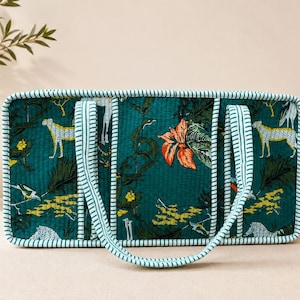 May include: A rectangular quilted tote bag in deep teal featuring a vibrant print of cheetahs, tropical foliage, and orange flowers. The bag has two long handles and edges trimmed with a white and teal striped fabric pattern.
