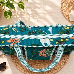 May include: A rectangular quilted tote bag in a deep teal color featuring a vibrant botanical print with orange flowers and white animals. The bag has a white zipper closure and two handles with a white and teal striped pattern.