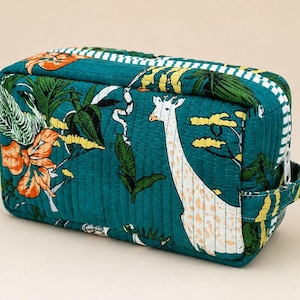 May include: A rectangular quilted toiletry bag in a deep teal color featuring a printed pattern of giraffes, orange flowers, and green tropical leaves. The bag includes a white and teal striped zipper trim and a matching side carry handle.