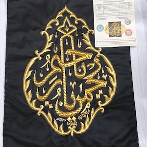 Pode incluir: Um painel de tecido preto com um intrincado bordado de fio dourado no centro, exibindo caligrafia árabe dentro de uma moldura oval pontiaguda. Um certificado de procedência branco está colocado no canto superior direito da imagem.
