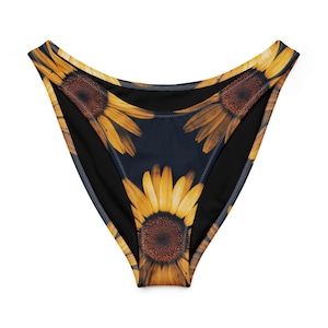 May include: High-waisted bikini bottoms featuring a dark navy blue background with a repeating sunflower pattern. The sunflowers have bright yellow petals and dark brown centers. The garment has a high-cut leg opening and visible stitching.