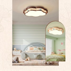 May include: A cloud-shaped flush mount ceiling light featuring a dark wood frame with cut-out details of small blue clouds and stars, surrounding a central white acrylic diffuser that emits a soft, even glow across the room's ceiling surface.