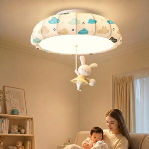 May include: A round ceiling light fixture featuring a fabric shade decorated with blue and tan cloud and star patterns. A white rabbit figurine wearing a yellow skirt hangs from the centre of the light, suspended by a thin white rod.