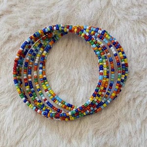 Peut inclure: Un bracelet multi-tours composé de petites perles de rocaille en verre aux couleurs vives, alternant le rouge, l'orange, le jaune, le vert, le bleu et le blanc. Cet accessoire circulaire présente une structure flexible formant plusieurs rangs.