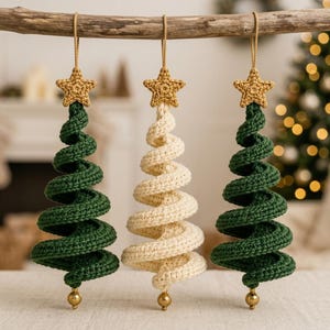 May include: Three hanging ornaments shaped like spiral Christmas trees. Two are dark green and one is cream-coloured. Each tree is topped with a small, crocheted gold star and features a single gold bead at the bottom point, suspended by a tan string.