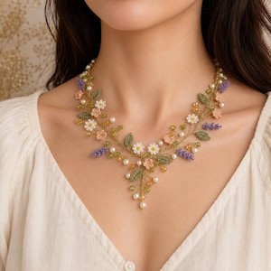 Può includere: Una collana floreale con delicati fiori all'uncinetto in bianco, pesca e lavanda, accentuati da foglie verdi, piccole perline gialle e perle bianche. L'intricato design è realizzato su una base di filo sottile e flessibile a forma di tralcio.