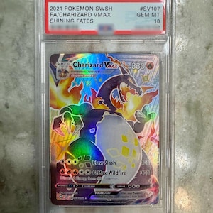 May include: A graded 2021 Pokemon SWSH Shining Fates Charizard VMAX trading card in a clear plastic slab. The card features a holographic illustration of a black Charizard with orange flames, 330 HP, and the attacks Claw Slash and G-Max Wildfire.