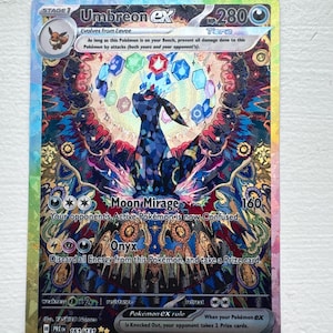 May include: A holographic Umbreon ex trading card featuring a stained-glass style illustration of the dark-type creature surrounded by floating colourful gems. The card displays the name, 280 HP, attacks Moon Mirage and Onyx, and set number 161/131.