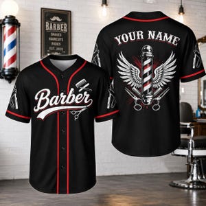 May include: A black baseball jersey with red trim, featuring the word Barber in white script on the front, a comb and scissors graphic, and a back design with a barber pole, wings, scissors, and the customizable text YOUR NAME in white.