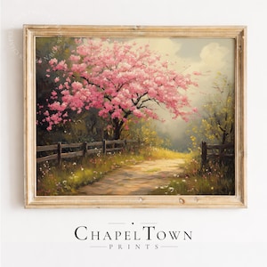 May include: A framed landscape painting featuring a large tree with vibrant pink blossoms standing beside a wooden fence. A dirt path winds through a grassy field with scattered wildflowers under a soft, cloudy sky. The frame is light-colored wood.