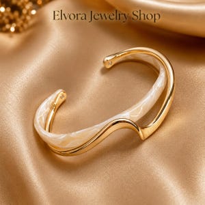 Gouden golfmanchetarmband, crèmekleurige armband van marmerhars, sculpturale open manchet, moderne luxe stijl