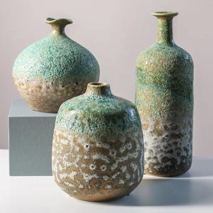 Könnte beinhalten: Drei Keramikvasen mit texturierten Oberflächen. Eine ist eine runde Vase mit kurzem Hals in Blaugrün und Hellbraun. Eine weitere ist breiter und niedriger mit blaugrünem Oberteil und hellbrauner, weiß gesprenkelter Basis. Die dritte ist eine hohe, schlanke Vase.