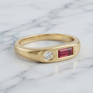 Peut inclure: Une bague en or avec un diamant blanc rond serti clos et un rubis rouge rectangulaire serti clos. L'anneau présente une finition lisse et polie avec un profil arrondi, mettant en valeur les deux pierres côte à côte horizontalement.