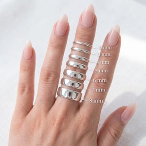May include: A series of seven polished silver-toned bands stacked on a finger, ranging in width from 2 mm to 8 mm. Each band is labelled with its corresponding width in millimetres, providing a clear visual comparison of the different sizes.