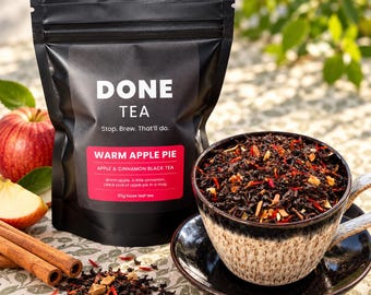 May include: A black pouch of Done Tea labeled Warm Apple Pie, Apple & Cinnamon Black Tea, 50g loose leaf tea. Next to it is a cup filled with dark tea leaves, red petals, and dried apple pieces, with cinnamon sticks and a fresh apple nearby.