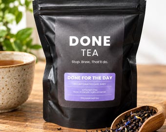 May include: A black stand-up pouch of Done Tea labeled Done For The Day Decaffeinated Earl Grey, 50g loose leaf tea. The label features the text Stop. Brew. That'll do. A wooden scoop filled with loose tea leaves sits in front.