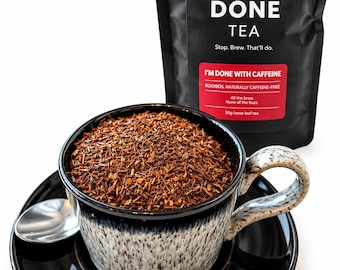 May include: A black and white speckled ceramic cup filled with loose leaf rooibos tea, resting on a matching saucer with a silver spoon. Behind it stands a black pouch labeled DONE TEA, I'M DONE WITH CAFFEINE, ROOIBOS, NATURALLY CAFFEINE-FREE, 50g.