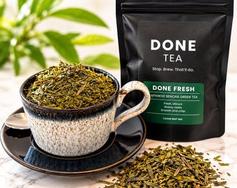 May include: A black pouch of Done Tea Japanese Sencha green tea with white text reading Done Tea, Stop. Brew. That'll do. A ceramic cup filled with loose green tea leaves sits on a matching saucer next to a pile of loose tea leaves.