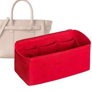 May include: Red felt bag organizer with multiple pockets for a handbag. The organizer has a zipper closure and is designed to fit inside a handbag to help keep it organized.