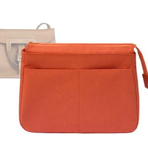May include: An orange handbag organiser with a zip closure and multiple pockets. The organiser is rectangular and designed to fit inside a larger bag. A light beige handbag is visible in the background.