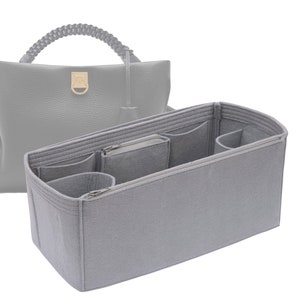以下が含まれることがあります： 複数のコンパートメントとジッパー付きポケットが付いたグレーのフェルト製バッグオーガナイザー。オーガナイザーはハンドバッグに収まるように設計されており、バッグを整理するのに役立ちます。