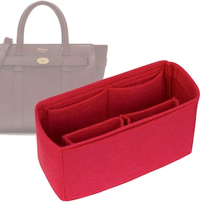 May include: Red felt bag organizer with multiple compartments for a handbag. The organizer has a rectangular shape and is designed to fit inside a handbag to help keep it organized.