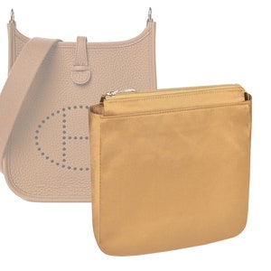 May include: A beige leather handbag with a perforated design and a gold zipper. The bag is shown with a beige fabric insert.