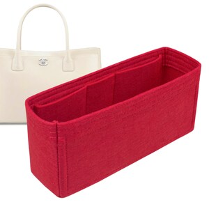 May include: Red felt bag organiser with multiple compartments for a handbag. The organiser has a rectangular shape and is made of a soft, felt material.