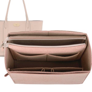 May include: A blush pink felt bag organizer with multiple pockets and a zippered compartment. The organizer is designed to fit inside a tote bag.