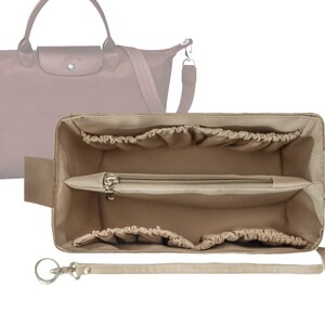 Könnte beinhalten: Beige Stofftasche Organizer mit mehreren Fächern und einer Reißverschlusstasche. Der Organizer hat einen Riemen und einen Schlüsselring.