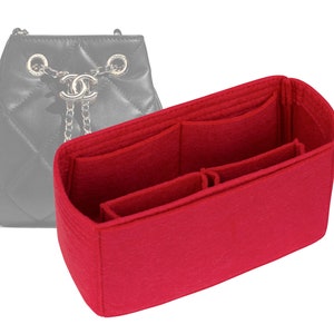 May include: Red felt bag organizer with multiple compartments for a handbag. The organizer has a rectangular shape and is designed to fit inside a larger bag.